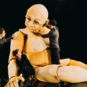 Trois personnes sur une scène de théâtre avec une marionnette géante.