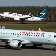 Un avion d'Air Canada qui atterrit, au premier plan; et en arrière-plan, un avion de WestJet qui décolle.