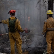 Deux personnes avec des pelles devant les braises d'un feu de forêt près de Hay River, le 22 août 2023. 