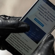 Une main qui tient un cellulaire avec un article sur le ChatGPT.