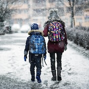 Deux enfants marchent vers l'école, avec un sac à dos dans un décor hivernal.