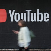 Une personne marche devant une publicité de la plateforme YouTube.
