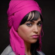 Une femme portant un turban rose, de trois quart profil, devant un fond noir.