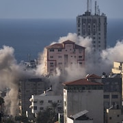 Au loin, la mer Méditérranée. En premier plan, des bâtiments desquels s'échappe de la fumée après une attaque aérienne.