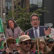 Des gens marchent dans la rue et tiennent des drapeaux et des images de Sonia Lebel et Bernard Drainville.