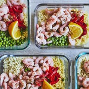 Des couscous aux crevettes, petit-pois, poivrons rouges et citron disposés dans des plats transparents.