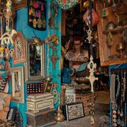 Un artisan est dans sa boutique, qui regorge de bijoux, de tableaux, de miroirs et de mains de Fatma. 