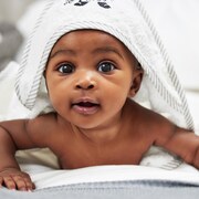 Un bébé étendu sur le ventre, avec une serviette sur la tête, regarde devant.