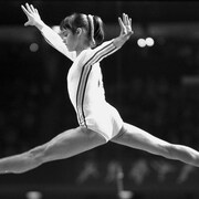 La gymnaste Nadia Comaneci saute en faisant le grand écart.