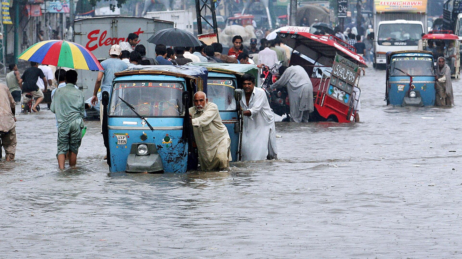 Des gens poussent leur voiture dans une rue inondée.