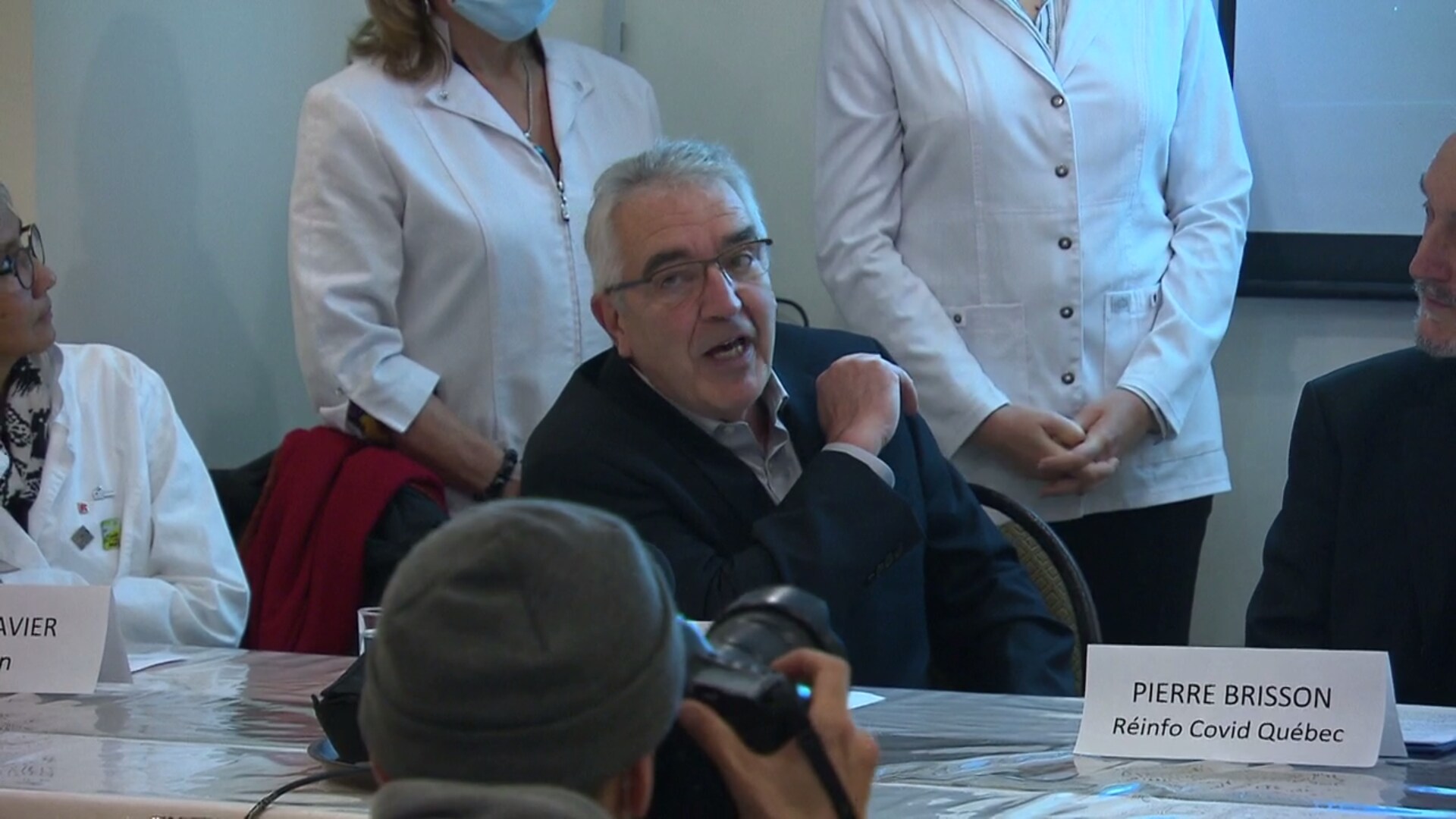 Le Dr Alain Roux s'adresse au public lors d'une conférence de presse. Il porte un veston et une chemise.