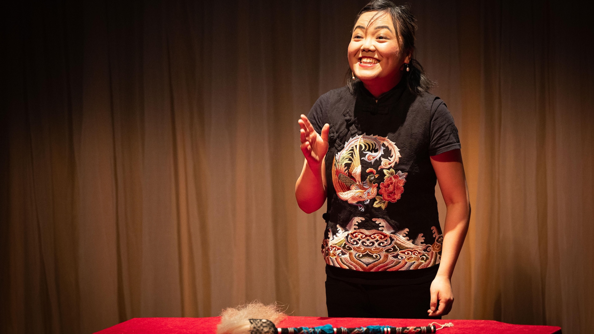 Aurore Liang sur une scène debout derrière une table sur laquelle est déposé un objet en forme de bâton. 