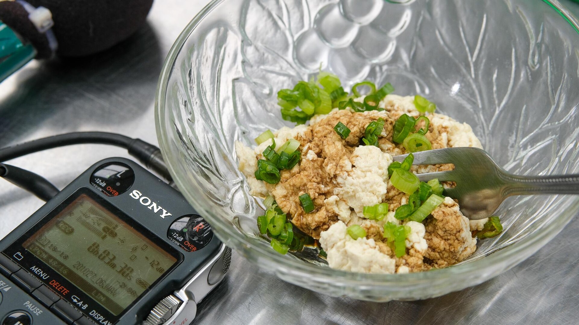 Du tofu fraîchement préparé dans un bol transparent déposé aux côtés d'un enregistreur numérique. Du tofu fraîchement préparé dans un bol transparent déposé aux côtés d'un enregistreur numérique.