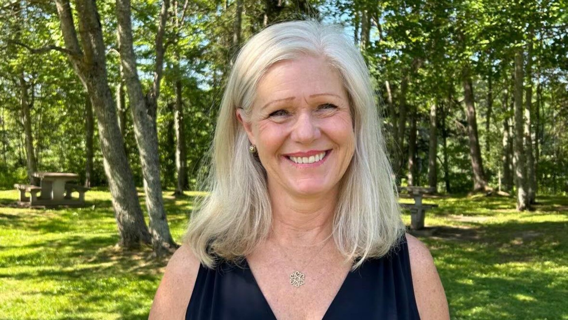 Dawn Arnold, dehors dans un parc en été, regarde directement la caméra et sourit pour une photo.