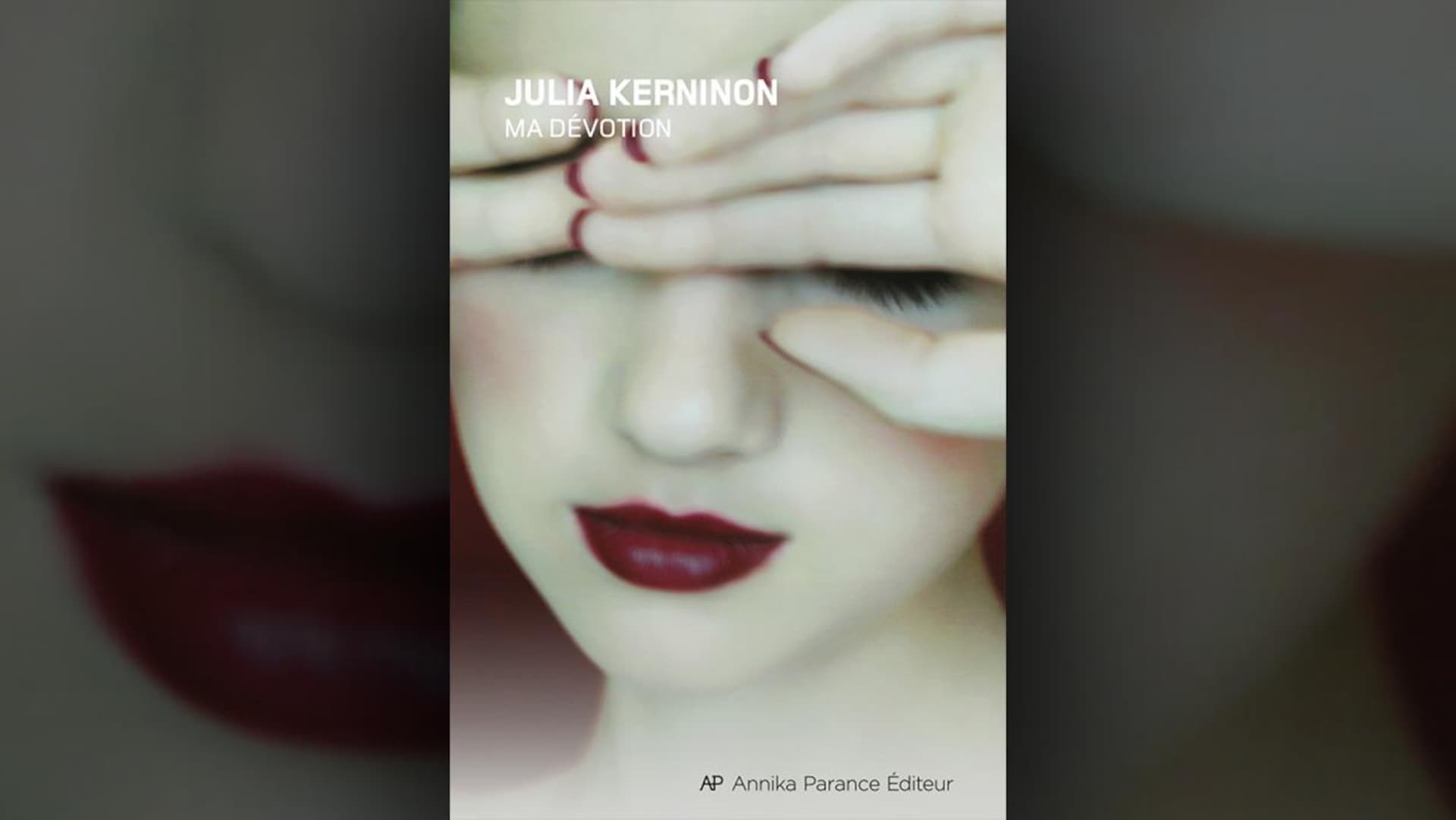 Sur la couverture du livre  Ma dévotion , de Julia Kerninon, il y a en arrière-plan la photo du visage d'une femme maquillée, les yeux fermés, les mains en partie couvrant ses yeux. Elle porte un vernis à ongles rouge et du rouge à lèvres rouge.