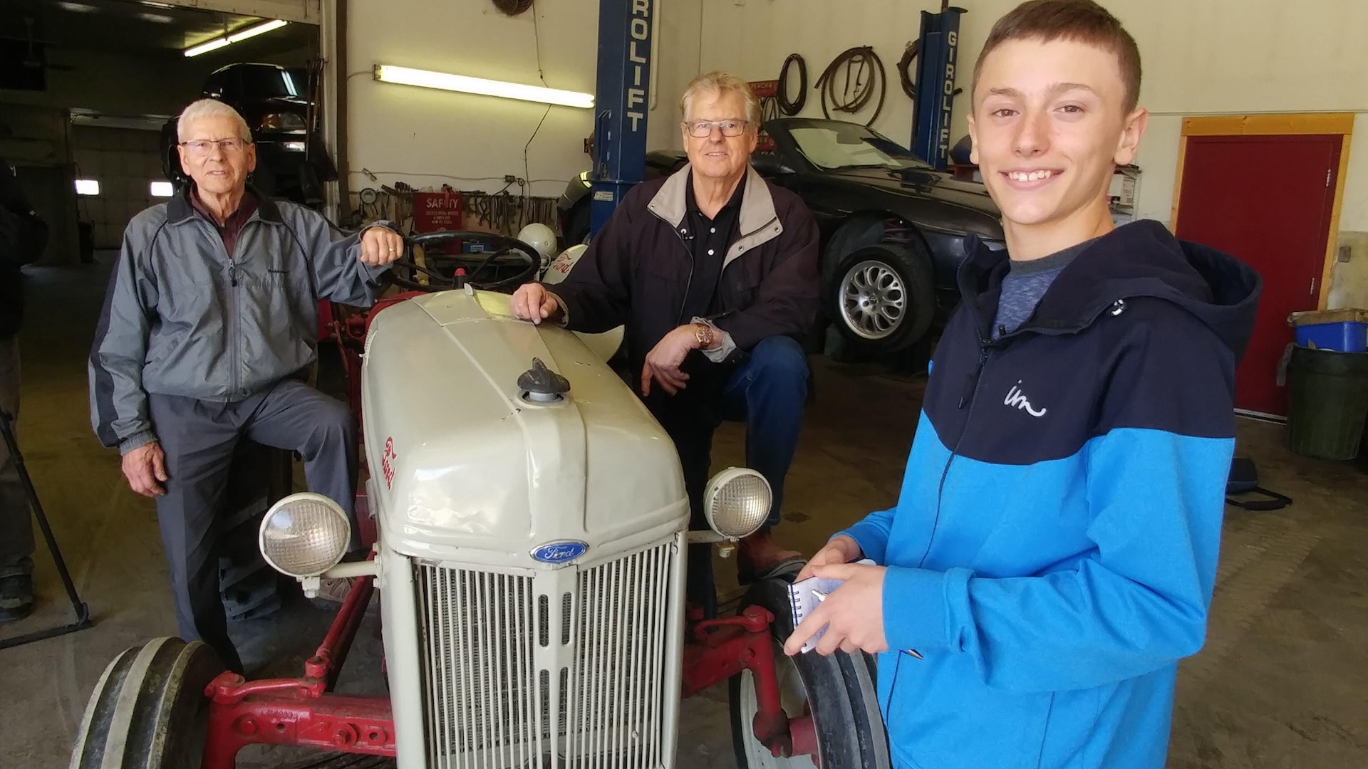 Élya Lavoie, René et Robert Lussier se tiennent debout près d'un vieux tracteur Ford. 