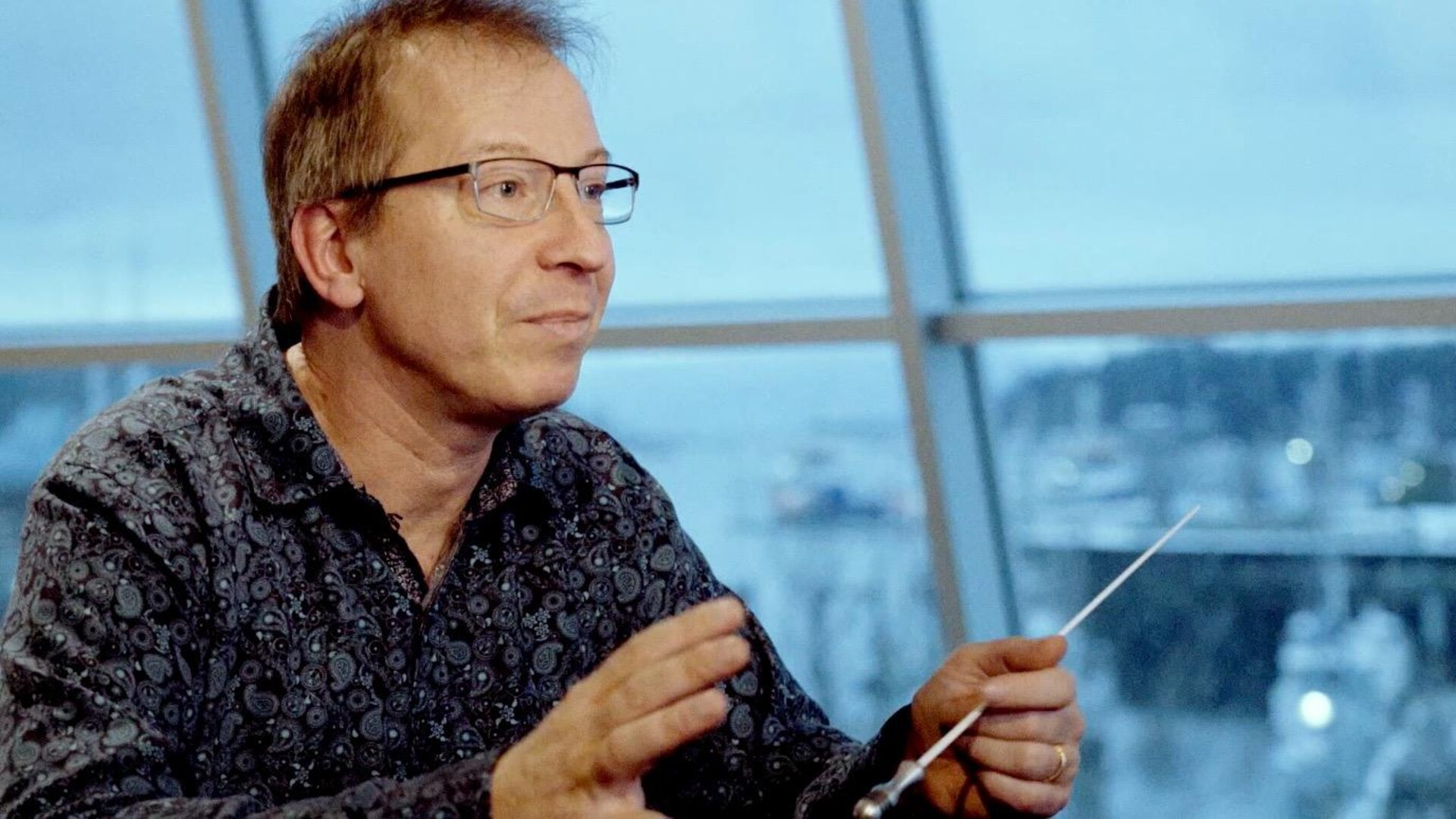 Pierre Simard, directeur artistique et musical du Vancouver Island Symphony, assis dans son bureau, tenant une baguette dans sa main gauche.