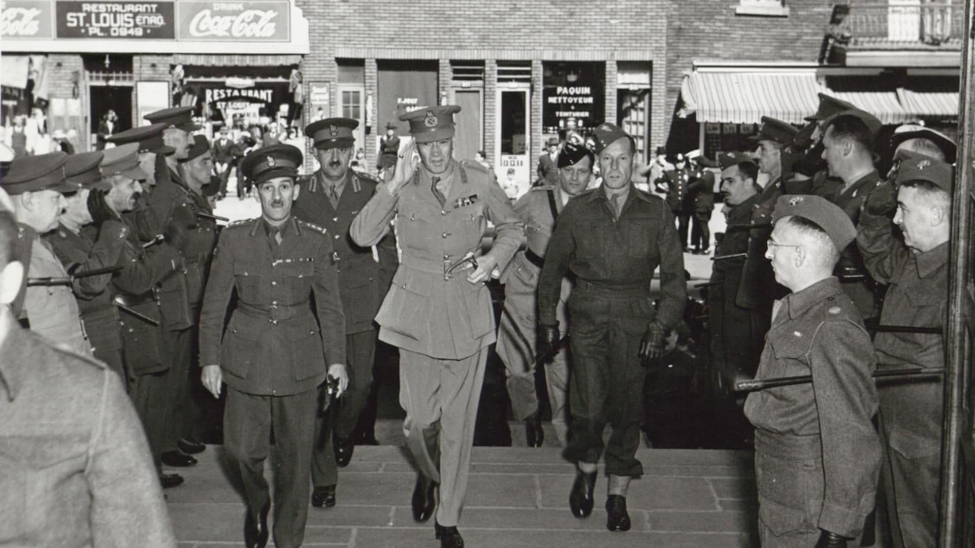 Des militaires en uniforme, vus de face, en train de gravir un escalier, dans un quartier populaire de Montréal. On les attend pour une cérémonie officielle dans une église. Le général marche tout en faisant le salut militaire. Des militaires en uniforme, vus de face, en train de gravir un escalier, dans un quartier populaire de Montréal. On les attend pour une cérémonie officielle dans une église. Le général marche tout en faisant le salut militaire.