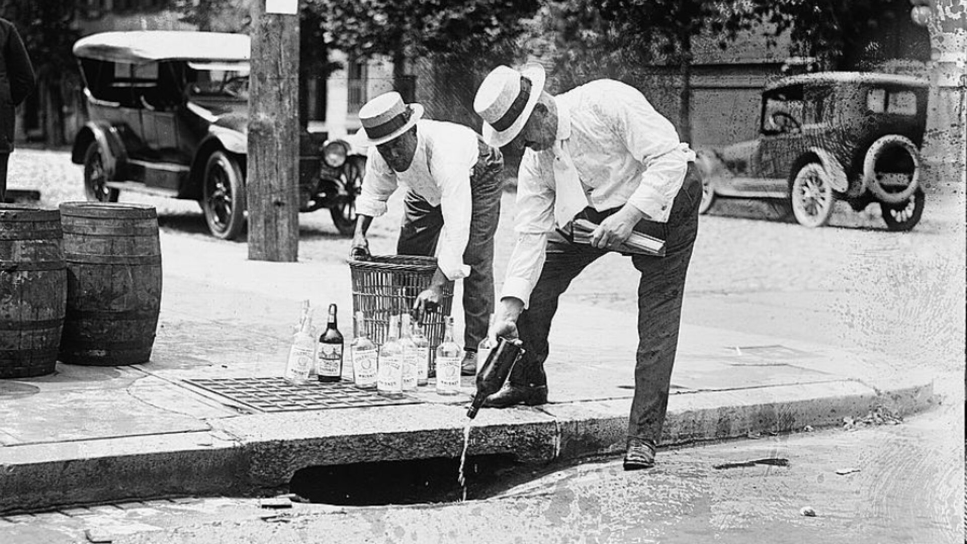 Des adeptes de la tempérance bien mis, en chemise blanche et en canotier, sont occupés à verser le contenu de plusieurs bouteilles d'alcool dans le caniveau, en pleine rue, aux États-Unis. Des adeptes de la tempérance bien mis, en chemise blanche et en canotier, sont occupés à verser le contenu de plusieurs bouteilles d'alcool dans le caniveau, en pleine rue, aux États-Unis.