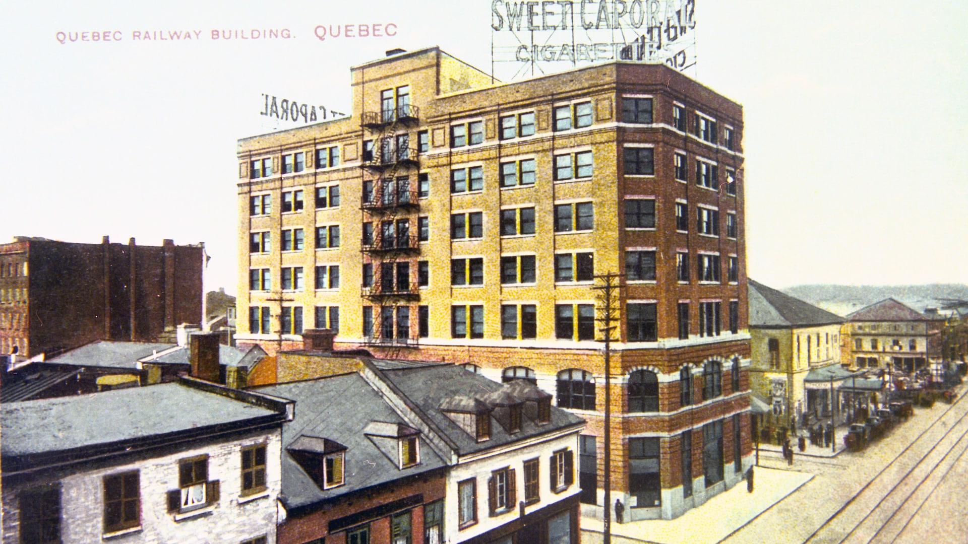 L'édifice de la Quebec Railway se trouve en plein centre-ville de Québec et domine la basse-ville depuis 1912. On voit les rails de tramway et des voitures, et l'édifice est dominé par une annonce de cigarettes Sweet Caporal. L'édifice de la Quebec Railway se trouve en plein centre-ville de Québec et domine la basse-ville depuis 1912. On voit les rails de tramway et des voitures, et l'édifice est dominé par une annonce de cigarettes Sweet Caporal.