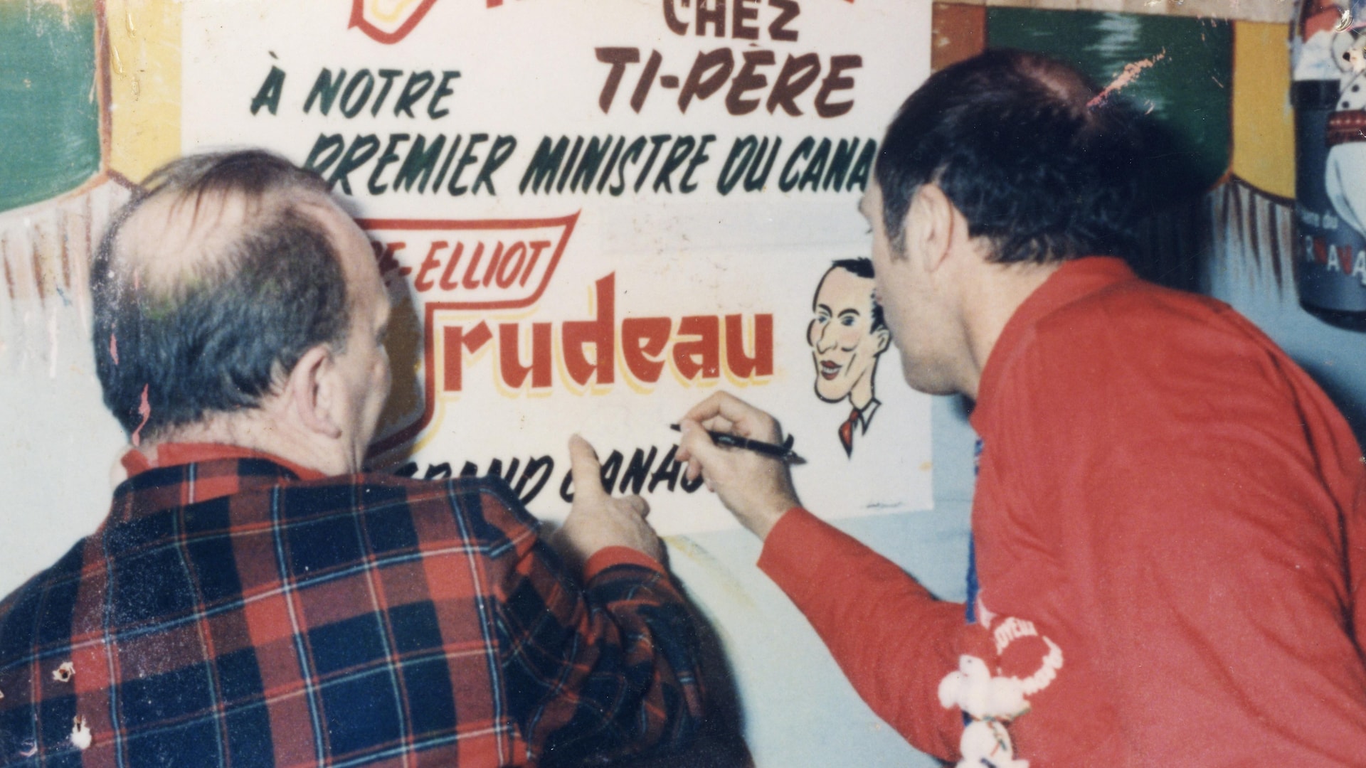 Le premier ministre Pierre Elliott Trudeau se prête au jeu de la signature souvenir en compagnie de Ti-Père, sur un grand panneau portant son nom, le nom des Voûtes et une caricature du célèbre premier ministre canadien.