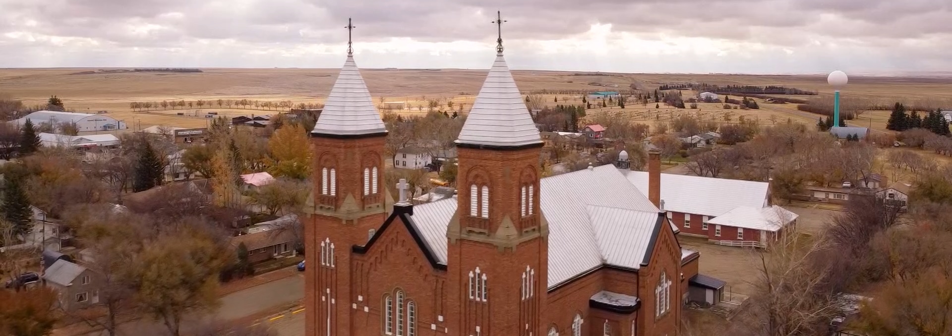 L'Église de Ponteix en Saskatchewan sous un ciel menaçant. On peut voir la tour à eau du village en arrière plan.
