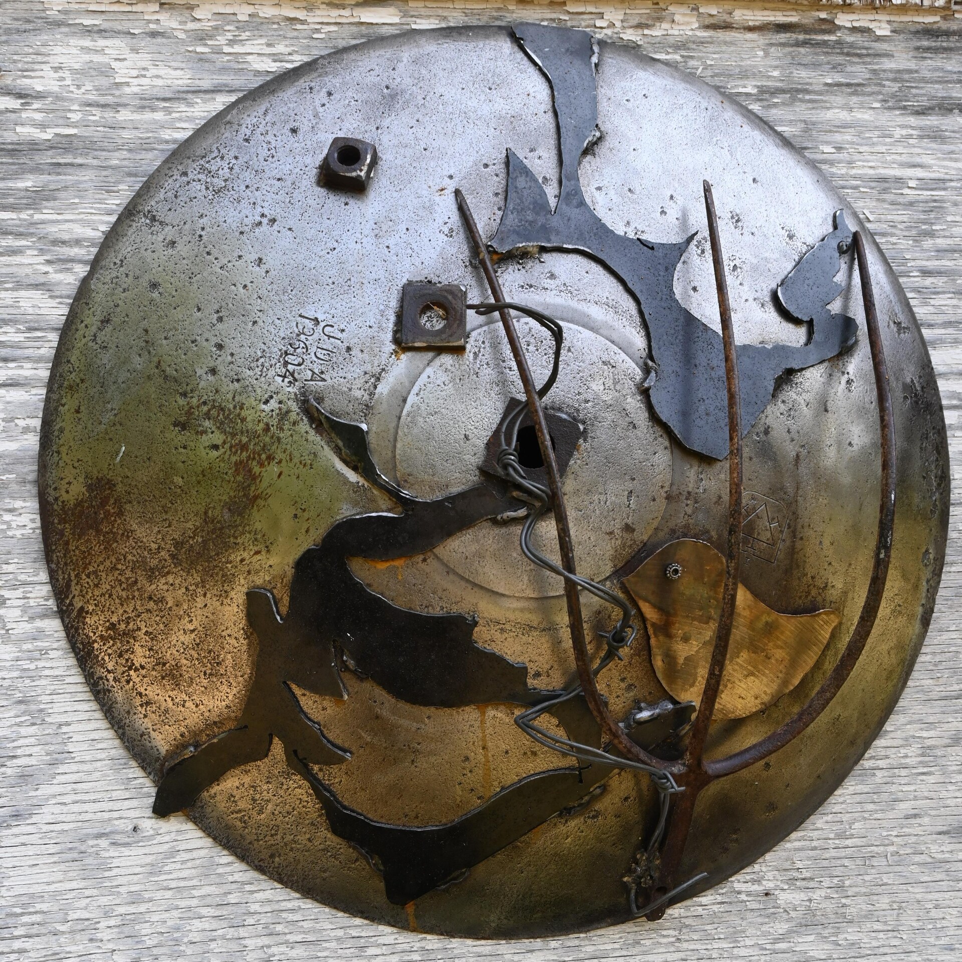 Sur un cercle en métal, l'artiste y a soudé quelques pièces en métal, dont une fourche, des boulons, de la broche et la découpure d'un oiseau.