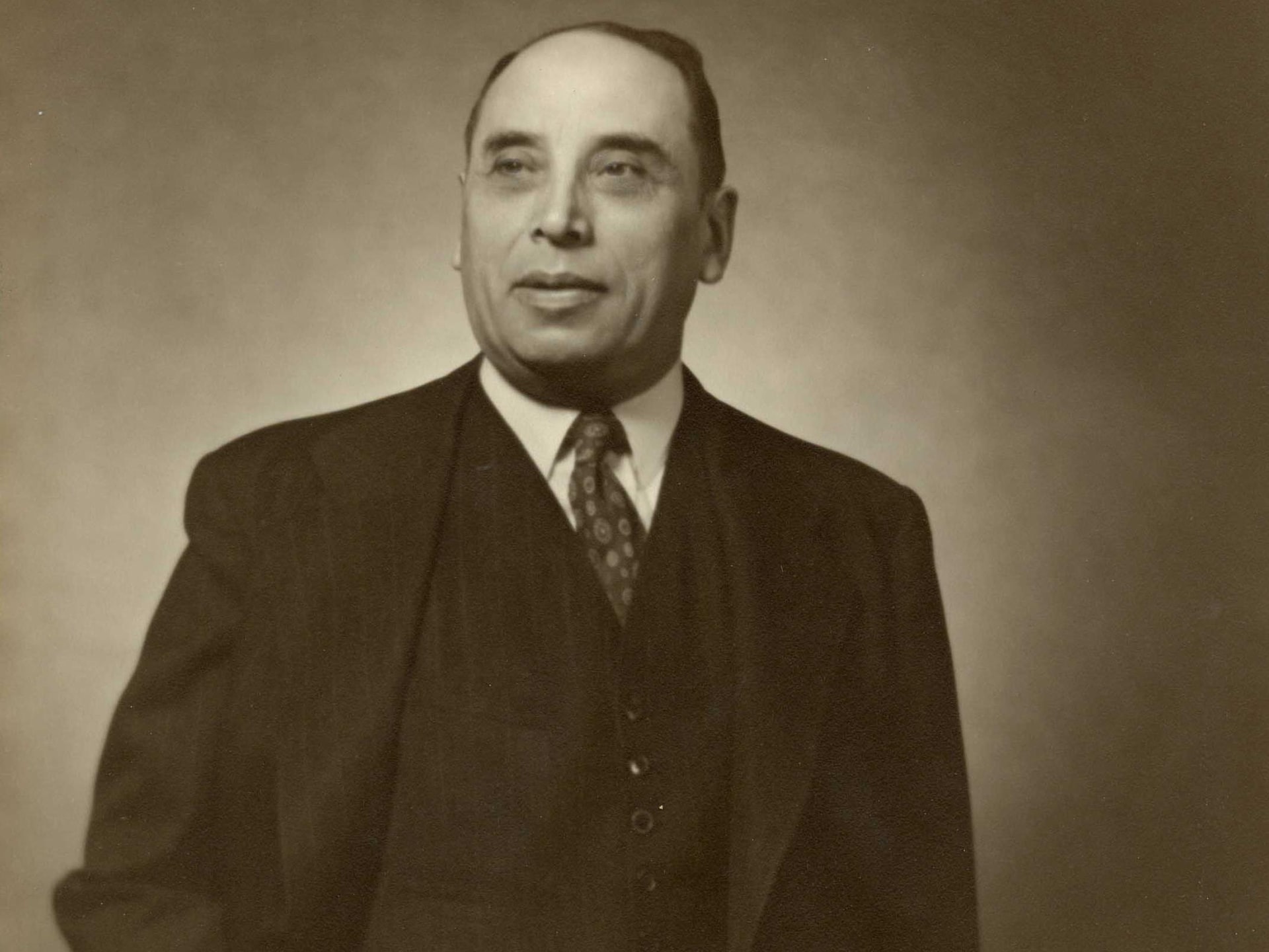 Portrait de Maurice Pollack, souriant, en complet cravate sur une image sépia typique des années 1960.