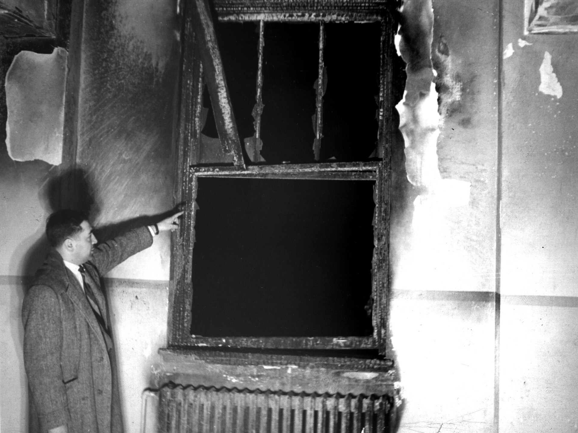Un homme pointe une fenêtre lourdement endommagée par un incendie après le sinistre de la synagogue de la rue Crémazie le 21 mai 1944.