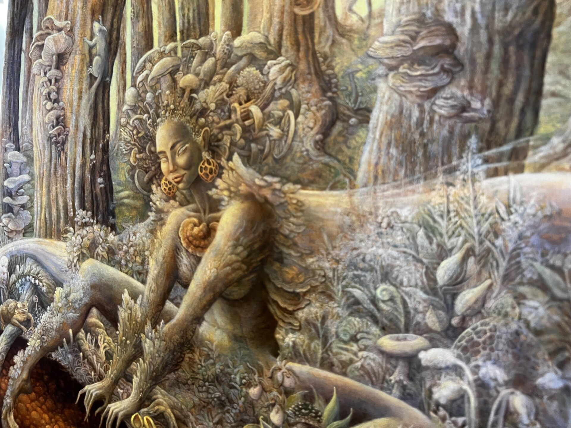 Sur une toile, un personnage féminin, la déesse des champignons. La déesse, qui est par terre, a une chevelure constituée de champignons de toutes sortes.
