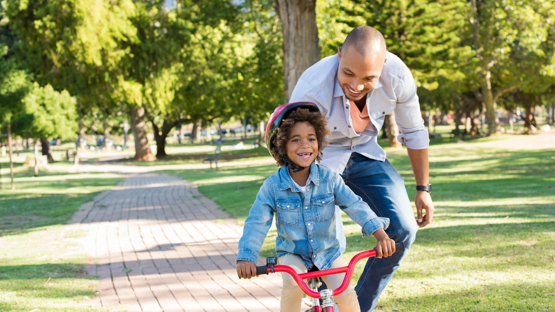 Un père apprend à son enfant à faire du vélo dans un parc.