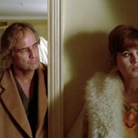 Marlon Brando et Maria Schneider sont debout l'un à côté de l'autre, en manteaux.