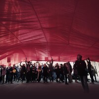 De jeunes étudiants sautent sous un drapeau rouge qui occupe toute la place au sommet de l'image.