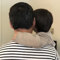 Un homme vu de dos tient son enfant dans ses bras.