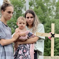 Deux jeunes femmes avec un bébé observent une croix fabriquée à la mémoire des victimes. 