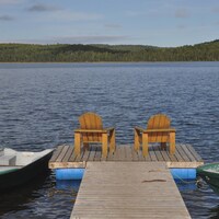 Deux chaises Adirondack se trouvent sur le quai d’un lac en Haute-Mauricie. Deux chaloupes flottent de chaque côté.