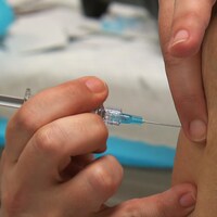 Plan rapproché sur la main d'une infirmière qui s'apprête à injecter une dose de vaccin dans le bras droit d'une dame âgée.