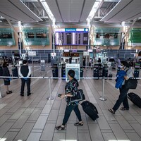 Des voyageurs, valises à la main, passent devant la zone d'enregistrement d'Air Canada dans un aéroport.