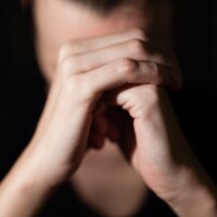 Une femme dont le visage est caché par ses mains en premier plan, paume droite sur poing gauche.
