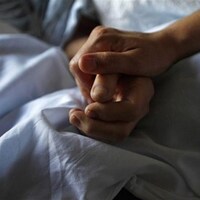 Deux mains posées sur un lit. 