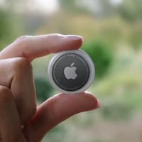 Une main qui tient un objet rond à l'effigie du logo d'Apple. 