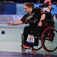 Une femme en fauteuil roulant qui lance une balle de boccia. 