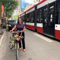 Alison Stewart debout devant un véhicule noir tient un vélo sur la chaussée à proximité d'un tramway.