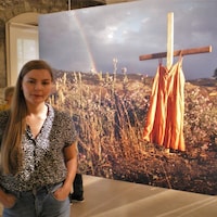Mains dans les poches, une jeune femme pose devant une photo en grand format dans une exposition.