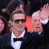 Brad Pitt sourit et fait un signe de la main sur un tapis rouge. 