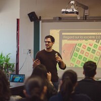 Charles-Antoine est devant un écran où est projetée une présentation destinée aux élèves, qui sont assis à leurs pupitres.