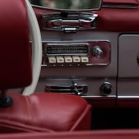 Dans une voiture ancienne, on voit l'appuie-tête rouge du siège en cuir et l'autoradio avec 5 gros boutons blancs.