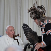 Un Autochtone portant une tenue traditionnelle munie de plumes s'adresse au pape qui est assis devant l'auditoire.