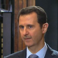 Bachar Al-Assad pose à côté d'un drapeau syrien.