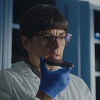 La femme, vêtue de gants bleus et d'une combinaison blanche pour éviter de contaminer une scène de crime, enregistre des notes vocales à l'aide d'un téléphone intelligent.